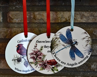 May include: Three round white ornaments with red, blue, and green ribbons. The ornaments feature a cardinal, a poinsettia, and a dragonfly with the text "Cardinals appear when Angels are near", "Ones we love don't go away they are always with us even when we can't see them", and "There are Angels among us".