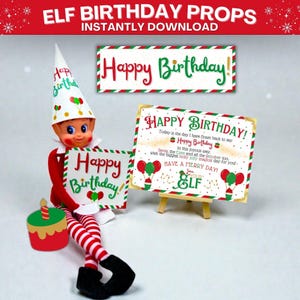 May include: An elf doll with a birthday theme. The elf is holding a sign that says "Happy Birthday!" and is wearing a hat with balloons. There is a small cake with a candle and other signs with birthday messages.
