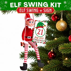 May include: An elf swing kit featuring a red and white striped swing suspended by ropes, holding a rectangular sign that reads 21 days until Christmas with a green elf hat graphic. The kit includes a sign and swing, but the elf doll is not included.