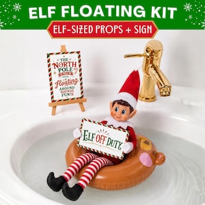 May include: An elf doll with a red and white hat and striped leggings sits in a brown bear-shaped inflatable ring. The doll holds a sign reading ELF OFF DUTY. A small wooden easel displays a sign reading THE NORTH POLE IS FULL OF WORK... FLOATING AROUND SOUNDS FUN.