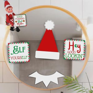 May include: A festive holiday-themed mirror decoration featuring a red and white Santa hat, a white mouth, and three signs with text: "Good Morning Stud Muffin", "Elf Yourself", and "Hey Good Lookin'". An elf figure is also present.