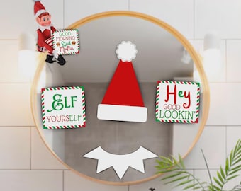 Könnte beinhalten: Festliche Weihnachtsdekoration für den Spiegel mit einem rot-weißen Weihnachtsmütze, einem weißen Mund und drei Schildern mit den Texten: "Good Morning Stud Muffin", "Elf Yourself" und "Hey Good Lookin'". Eine Elfenfigur ist ebenfalls vorhanden.