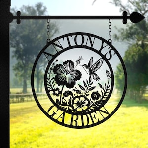 May include: Black metal garden sign with a circular design featuring a hummingbird and flowers. The sign reads "Tony's Garden".