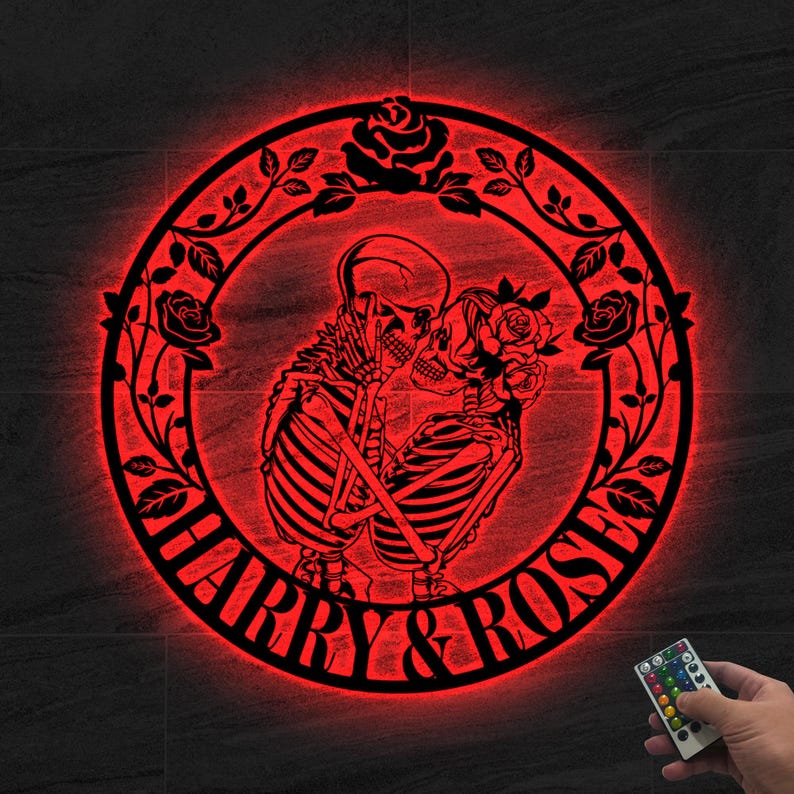 May include: A red, circular wall art piece featuring a skeleton couple embracing, surrounded by a floral wreath. The words "HARRY & ROSE" are inscribed at the bottom. A remote control is visible.