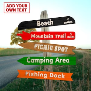 Puede incluir: Un poste de madera con múltiples señales direccionales. Las señales indican la playa, la ruta de montaña, el lugar de picnic, el área de acampada y el muelle de pesca. El poste tiene el texto "Add Your Own Text" en la parte superior.