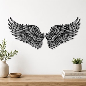 Könnte beinhalten: Schwarze Metall-Wandkunst, die ein Paar stilisierter Engelsflügel darstellt. Die Flügel sind detailliert mit geschichteten Federn, was ein strukturiertes Aussehen erzeugt. Geeignet als dekoratives Element für die Inneneinrichtung.