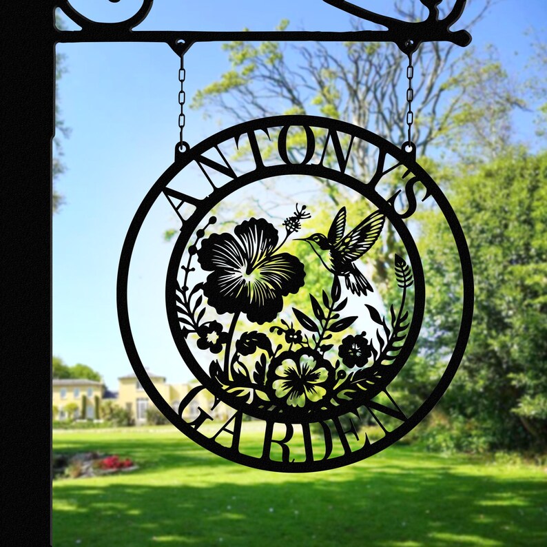 May include: Black metal garden sign with the text "ANTON'S GARDEN" in a circle. The sign features a hummingbird and floral designs.
