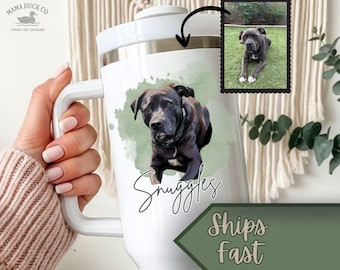 May include: A white stainless steel tumbler with a handle featuring a custom watercolor-style illustration of a dark-coated dog. Below the dog, the name Snuggles is written in black script. A small inset photo shows the dog on grass.