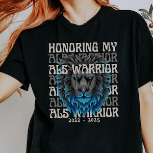 May include: Black t-shirt featuring a lion's head with blue and gray accents. The text "HONORING MY ALS WARRIOR" is stacked above the lion, with "2022-2025" below. The shirt is a short-sleeved crew neck.