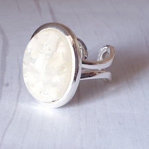 May include: A silver ring with a white oval-shaped stone set in a bezel setting.