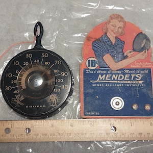 May include: A black and gold round dial thermometer with a string attached. The dial reads from 10 to 120 degrees. The thermometer is labeled "Cooper". The image also shows a vintage advertisement for "Mendets" a product that mends leaks instantly.