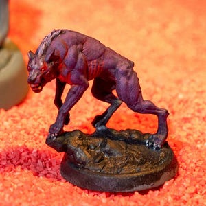 Puede incluir: Una pequeña miniatura de un hombre lobo pintada de morado y negro, de pie sobre una base negra. El hombre lobo está gruñendo con la boca abierta y los dientes al descubierto.