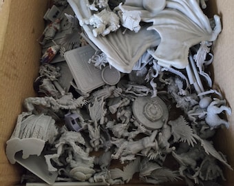 Op de afbeelding: Een doos gevuld met ongeverfde grijze plastic miniatuurfiguren, waaronder draken, ridders en andere fantasiewezens. De figuren zijn klaar om te worden geassembleerd en geschilderd.