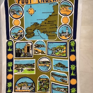 May include: A vintage tea towel depicting a map of Cornwall, England, with illustrations of coastal scenes and landmarks. The towel has a navy blue and olive green border with the text "The Foot of England".