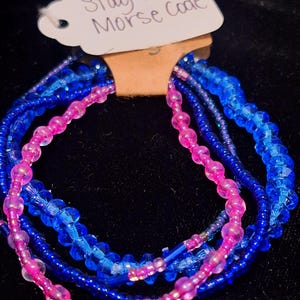 May include: A set of four beaded bracelets in pink and blue. The bracelets are stacked on top of each other and have a tag that reads "Stay Weird Morse Code".