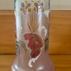 May include: A frosted glass vase with floral and leaf designs. The vase features pink, gold, and white accents. The flowers have pink petals and gold centers. The leaves are a mix of red, green, and gold. The vase has a rounded base and a cylindrical body.