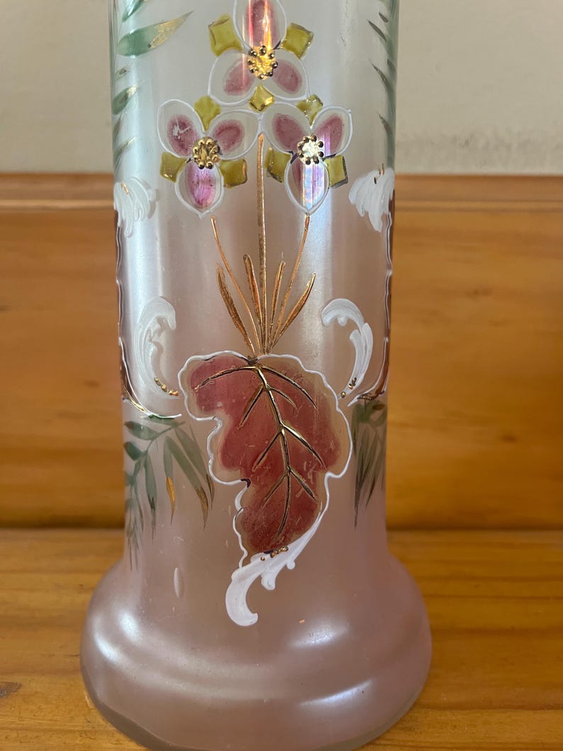 May include: A frosted glass vase with floral and leaf designs. The vase features pink, gold, and white accents. The flowers have pink petals and gold centers. The leaves are a mix of red, green, and gold. The vase has a rounded base and a cylindrical body.