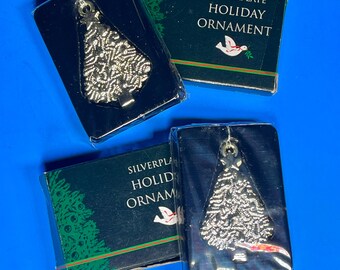 May include: Silverplate holiday ornaments in the shape of a Christmas tree. The ornaments are silver and come in a black box with the words "Silverplate Holiday Ornament" printed on the front. The background is a bright blue.
