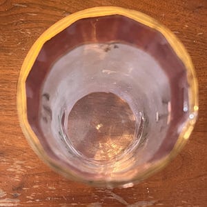 May include: A clear glass with a yellow and maroon rim. The glass is empty and sits on a wooden surface. The glass is viewed from above, showing its circular shape and the details of the rim.