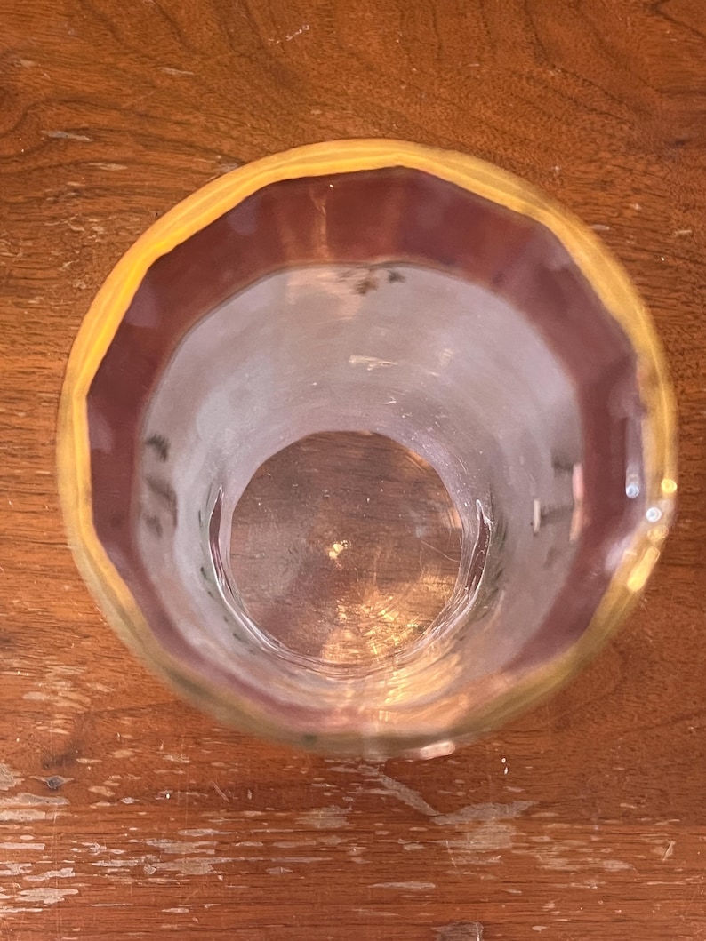 May include: A clear glass with a yellow and maroon rim. The glass is empty and sits on a wooden surface. The glass is viewed from above, showing its circular shape and the details of the rim.