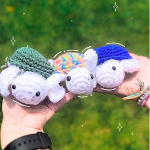 May include: Three crocheted turtle toys. One is green, one is rainbow colored, and one is blue. The turtles are all white with black eyes.