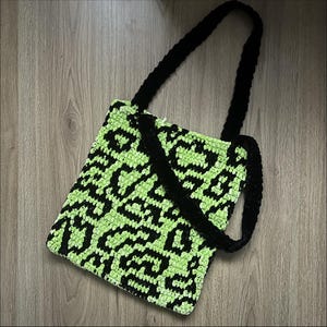 Puede incluir: Bolso tote de crochet hecho a mano con un estampado de leopardo verde neón y negro. El bolso tiene forma rectangular con asas negras. El bolso está hecho de un hilo suave y texturizado.