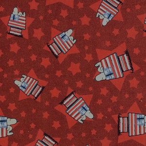 May include: Red fabric with a repeating pattern of white stars and a cartoon dog sitting in a doghouse with an American flag design. The doghouse is on a red platform.