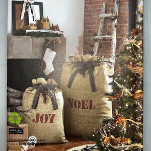 May include: A Simplicity sewing pattern for making Christmas decorations. The pattern shows two burlap sacks with the words "JOY" and "NOEL" printed on them. There is also a small Christmas tree with lights and a wooden ladder.