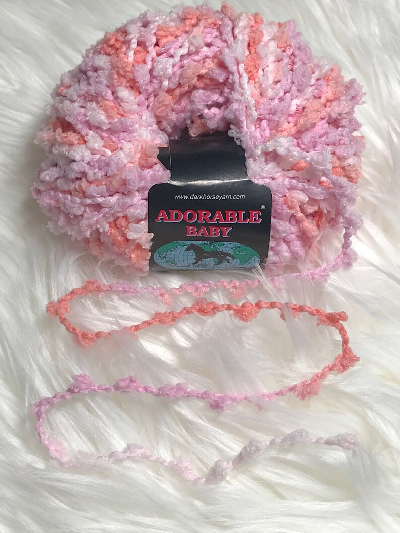 May include: A skein of pink, white, and peach yarn with a label that reads "Adorable Baby" and "www.darkhorseyarn.com".