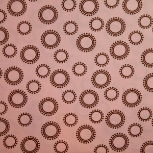 May include: A pink fabric with a repeating pattern of brown circles with a dotted border.