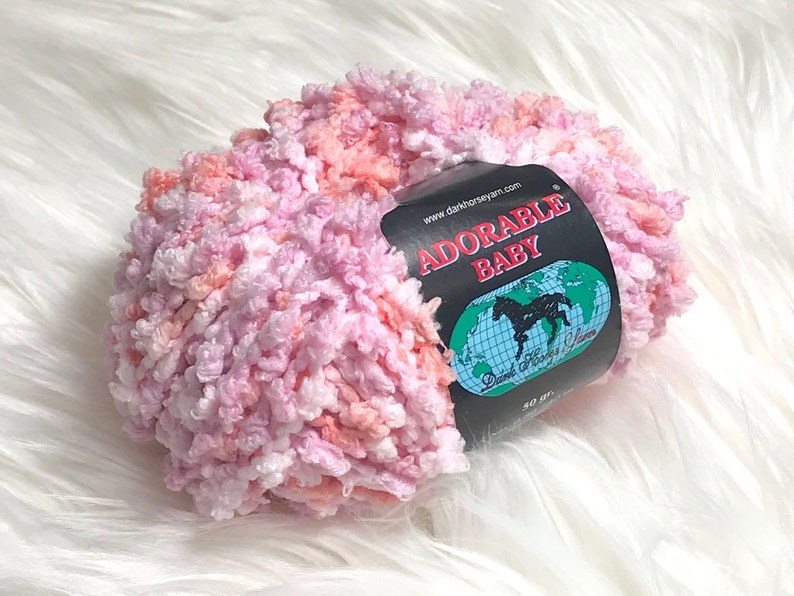 May include: A skein of pink, white, and peach yarn labeled "Adorable Baby" with the website address "www.darkhorseyarn.com".