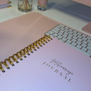 May include: A pink spiral bound journal with gold lettering that reads "The Miscarriage Journal".