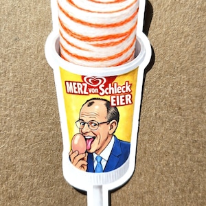 May include: A sticker depicting a cartoon ice cream treat with a red and white swirl. The container has a yellow background with the text "MERZ von Schleck EIER" and a cartoon of a man holding an egg.