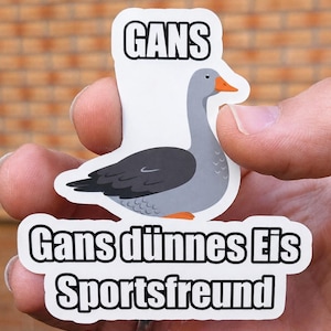 May include: A die-cut sticker featuring a grey goose with an orange beak. Above the goose is the text GANS, and below the goose is the text Gans dünnes Eis Sportsfreund. The sticker has a white border and a matte finish on the surface.