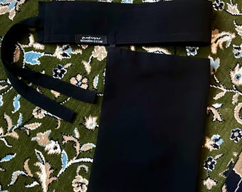 May include: A black belt with long ties and a matching black rectangular piece. The belt has the text "BEDOON ESSM" in white. The items are displayed on a green floral patterned rug.