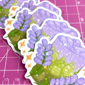 Puede incluir: Cuatro pegatinas de una bebida morada y verde con flores de lavanda y purpurina. La bebida est&aacute; en un vaso transparente con una pajita. Las pegatinas est&aacute;n en una estera de corte rosa.