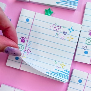May include: White sticky notes with blue lines and doodles, including hearts, stars, and cat faces. A hand is peeling back a note, revealing the lined paper. A green star-shaped paper clip is visible.