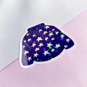 K&ouml;nnte beinhalten: Ein blauer und wei&szlig;er, schimmernder Aufkleber mit einem Pullover mit Sternenmuster.