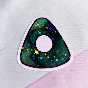 K&ouml;nnte beinhalten: Ein gr&uuml;ner holografischer Ouija-Planchette-Aufkleber mit einem wei&szlig;en Kreis in der Mitte und einem schwarzen Umriss.