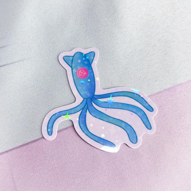 K&ouml;nnte beinhalten: Ein blauer, schimmernder Aufkleber mit einer Cartoon-Oktopus mit einem rosa Knopf als Auge. Der Oktopus hat sechs Tentakel und ist von schimmernden, regenbogenfarbenen Sternen umgeben.
