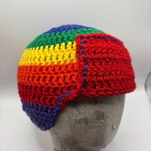 Peut inclure: Un chapeau crocheté fait à la main aux couleurs de l'arc-en-ciel : rouge, orange, jaune, vert, bleu et violet. Le chapeau a des cache-oreilles et est présenté sur une tête de mannequin. Le chapeau est en fil doux.
