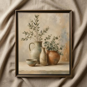 May include: A framed wall art print depicting a still life with a large light blue pitcher, a tall beige vase, a small bowl, and a terracotta pot. Green olive branches and eucalyptus leaves are arranged in the vessels against a textured background.