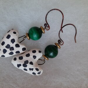 May include: A pair of earrings with white and black polka dot heart-shaped charms and green gemstone beads.