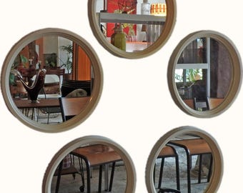 Könnte beinhalten: Set aus fünf runden Spiegeln mit hellen Holzrahmen. Die Spiegel reflektieren verschiedene Innenszenen, darunter Möbel und Pflanzen. Die Rahmen haben ein schlichtes Design, das für verschiedene Einrichtungsstile geeignet ist. Jeder Spiegel hat einen Durchmesser von ca. 20 cm.