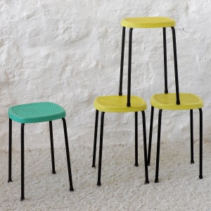 Puede incluir: Cuatro taburetes apilables con patas de metal negro. Los dos taburetes superiores son amarillos y los dos taburetes inferiores son verdes.