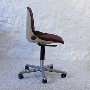 May include: A white and brown office chair with a swivel base and five wheels. The chair has a brown fabric seat and a white plastic back.