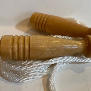 May include: A wooden jump rope with white rope and two wooden handles. The handles have a smooth, polished finish and are designed with a grooved pattern.