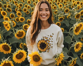 Könnte beinhalten: Ein weißer Pullover mit einem Sonnenblumen- und Schmetterlingsmotiv. Die Sonnenblume ist gelb mit brauner Mitte und die Schmetterlinge sind gelb. Der Pullover wird von einer Person getragen, die in einem Sonnenblumenfeld steht.