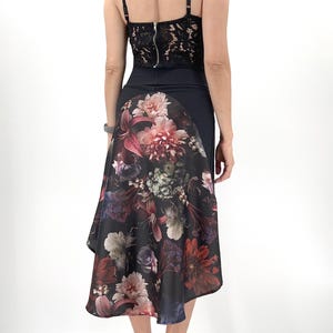 Könnte beinhalten: Schwarzes Spitzentop mit Spaghettiträgern und Reißverschluss. Der Rock ist schwarz mit einem Blumendruck in Rosa-, Rot- und Lilatönen. Der Rock hat einen asymmetrischen Saum. Das Model trägt goldene Absätze.