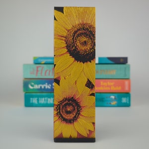 May include: A bookmark with a design of two yellow sunflowers with black centers. The sunflowers are on a red background.
